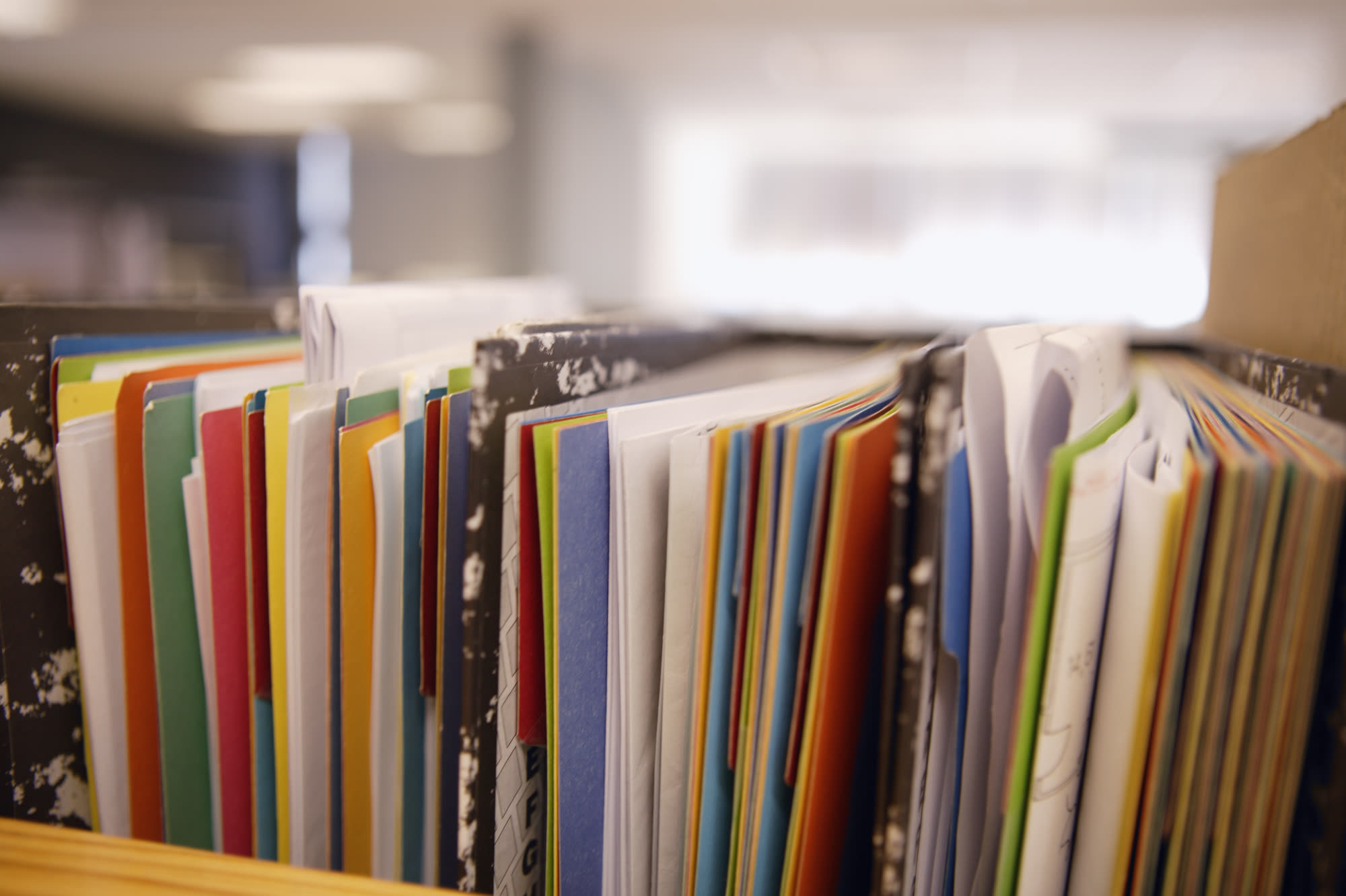 A packed row of coloured card folders and loose papers standing upright in an office file rack