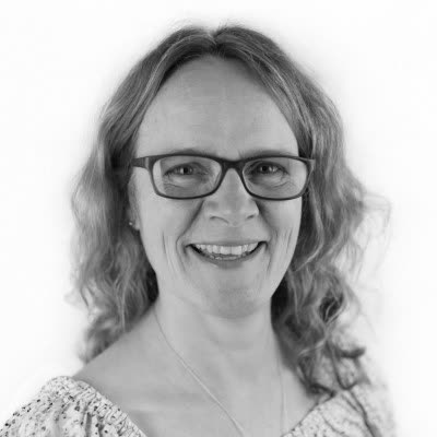 Black and white portrait of Elizabeth Brannon, smiling, in dark-framed glasses and a patterned top