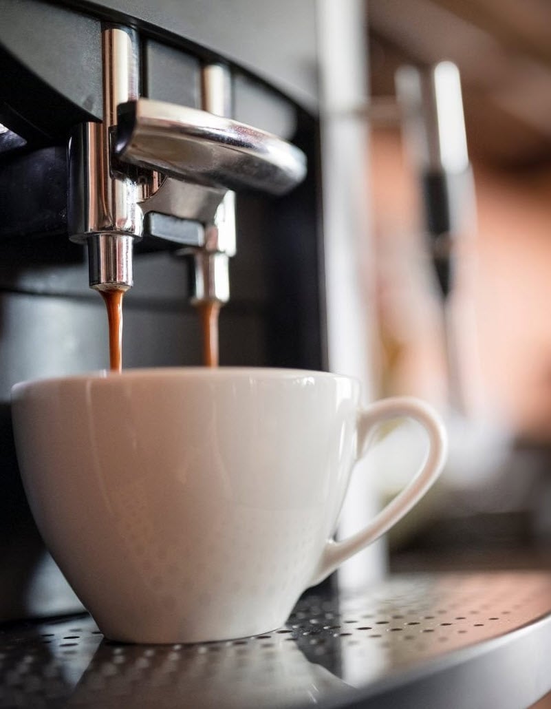Espresso pouring from a commercial machine into a white cup