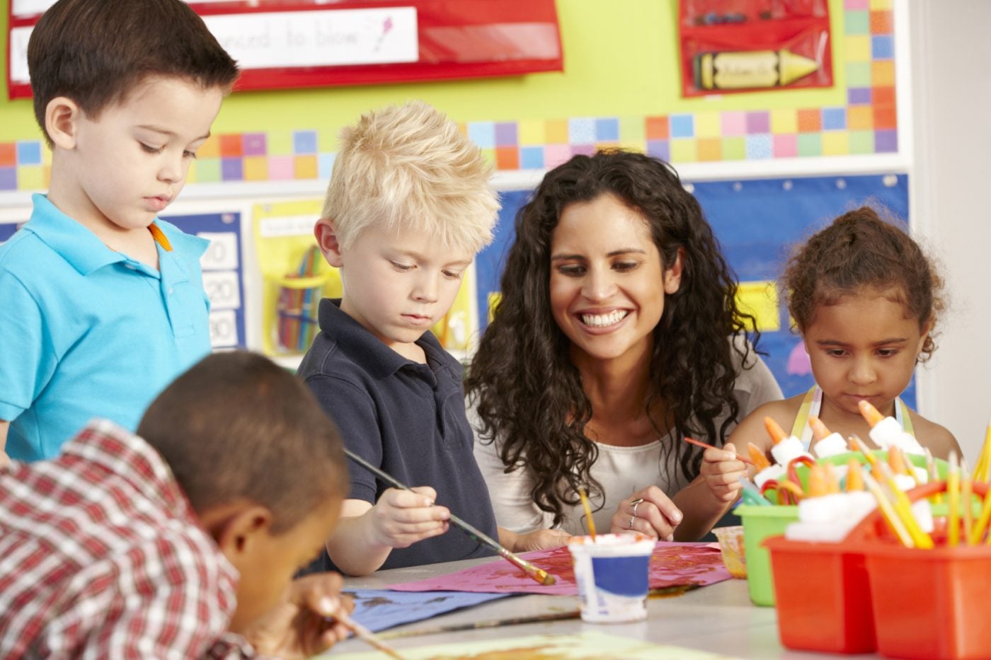 A teacher smiling with young children painting at a classroom table