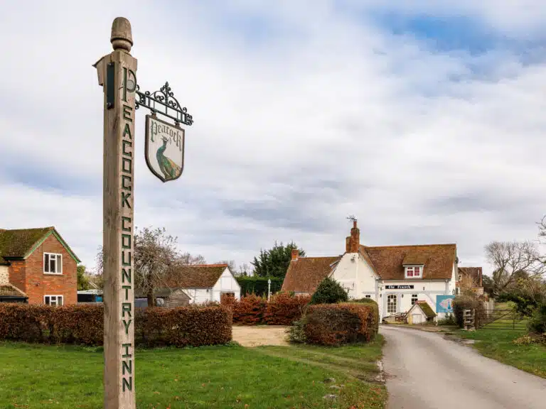 The Peacock Country Inn signpost, with the whitewashed inn and its lane behind