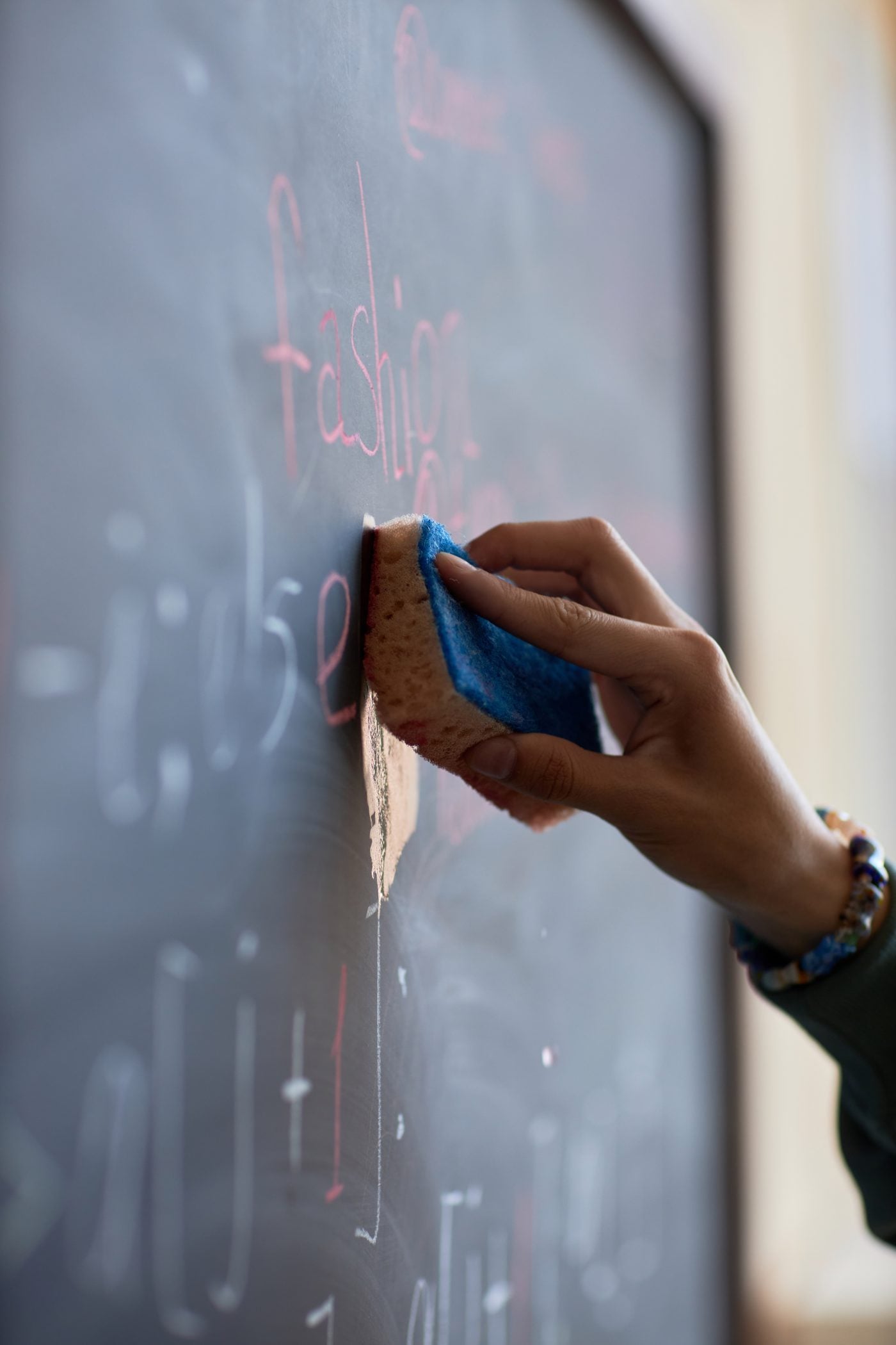 A hand erasing a chalkboard with a sponge in a classroom