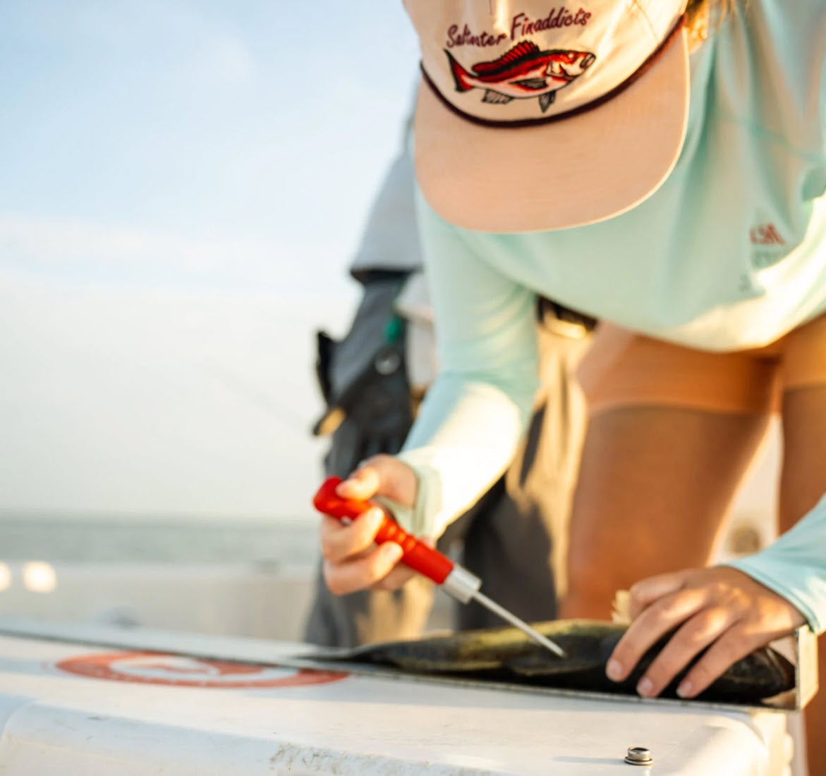 Angler on a boat unhooking a fish with a red Toit tool