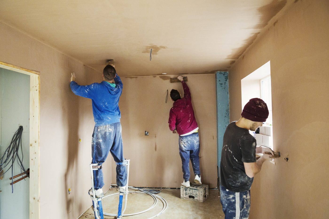Three plasterers skimming a room mid-renovation
