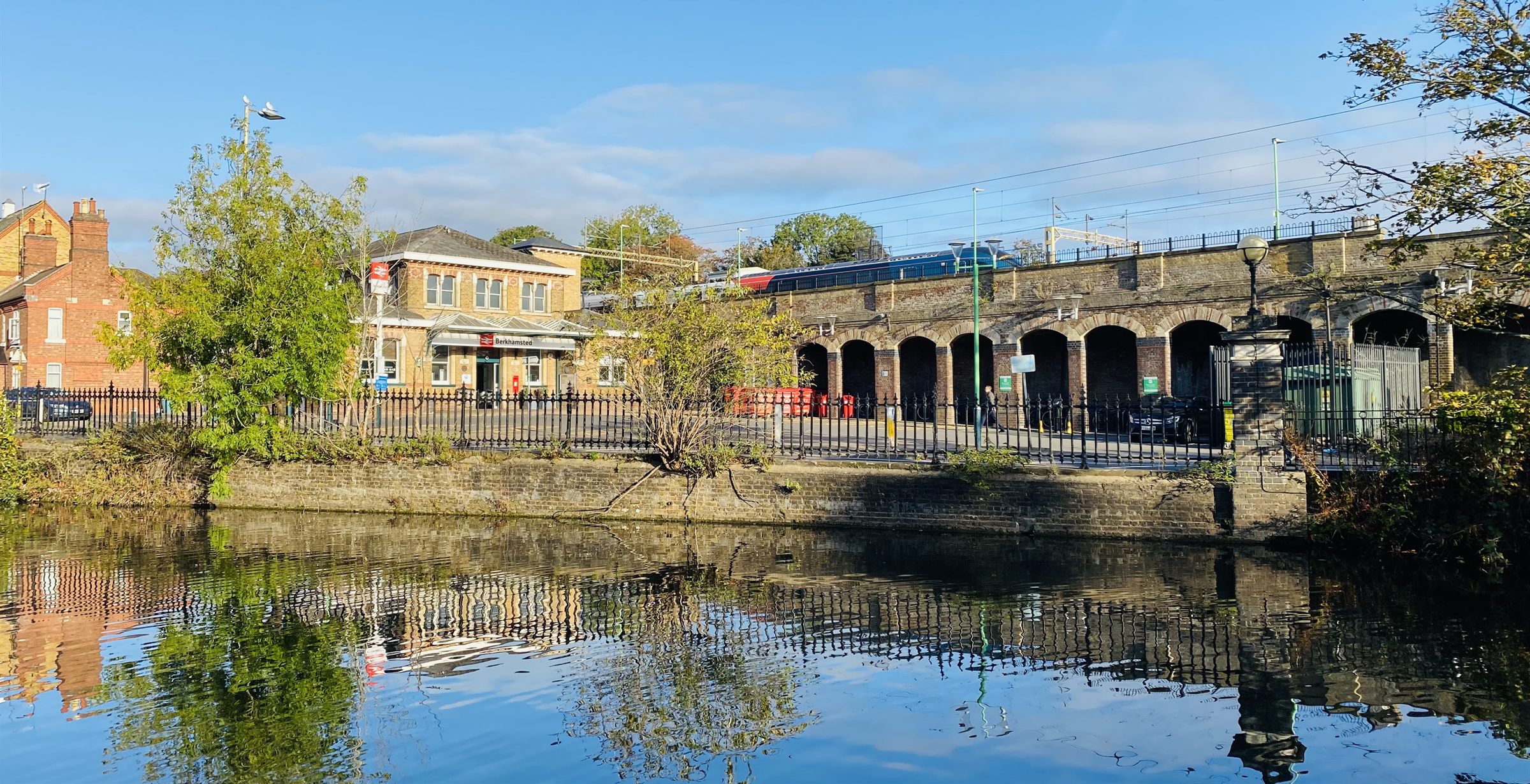 Berkhamsted station and the railway arches seen across still water, the buildings and trees reflected on a clear morning