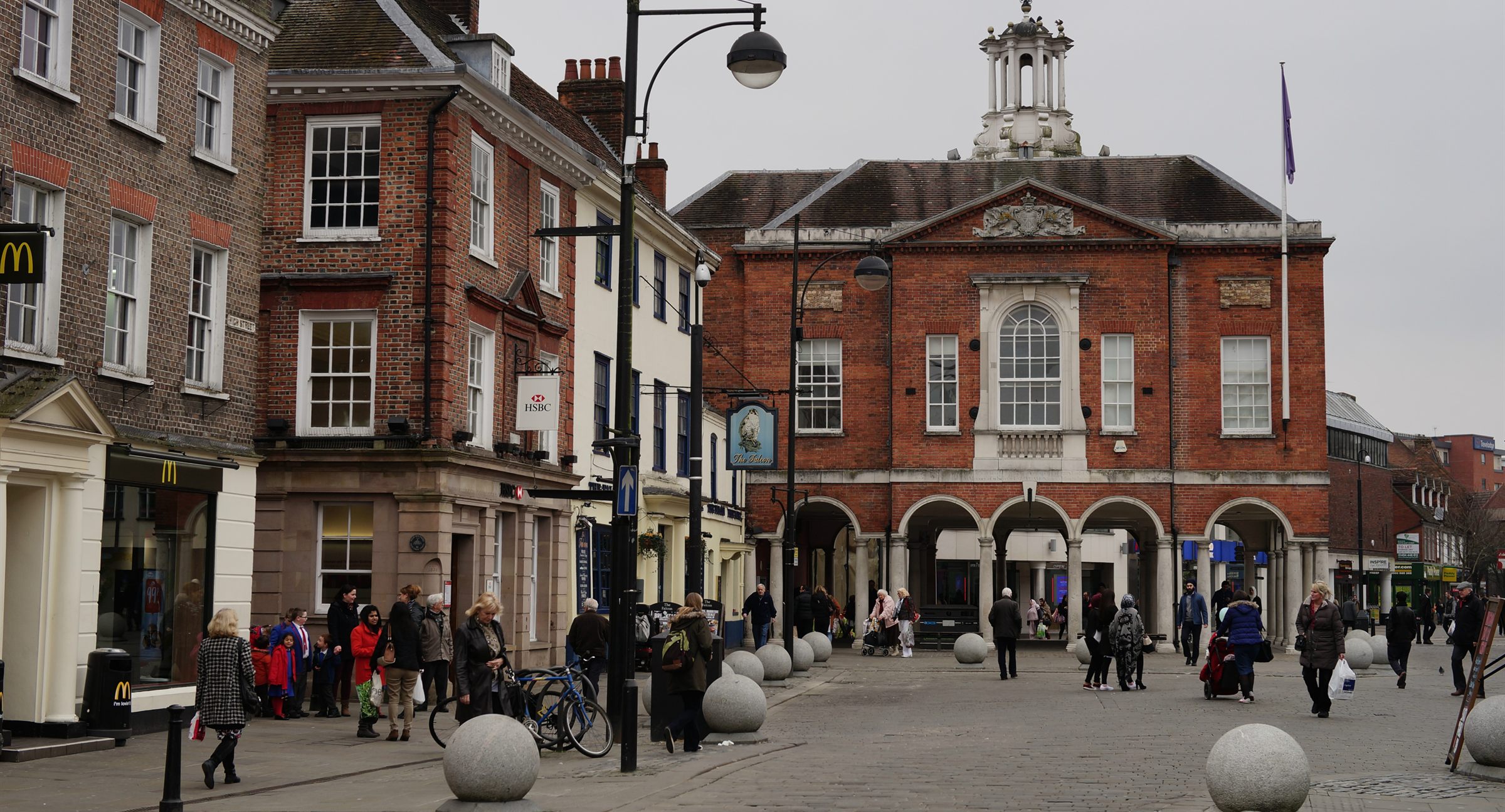 High Wycombe high street with shoppers passing the arched red-brick Little Market House under its white lantern roof