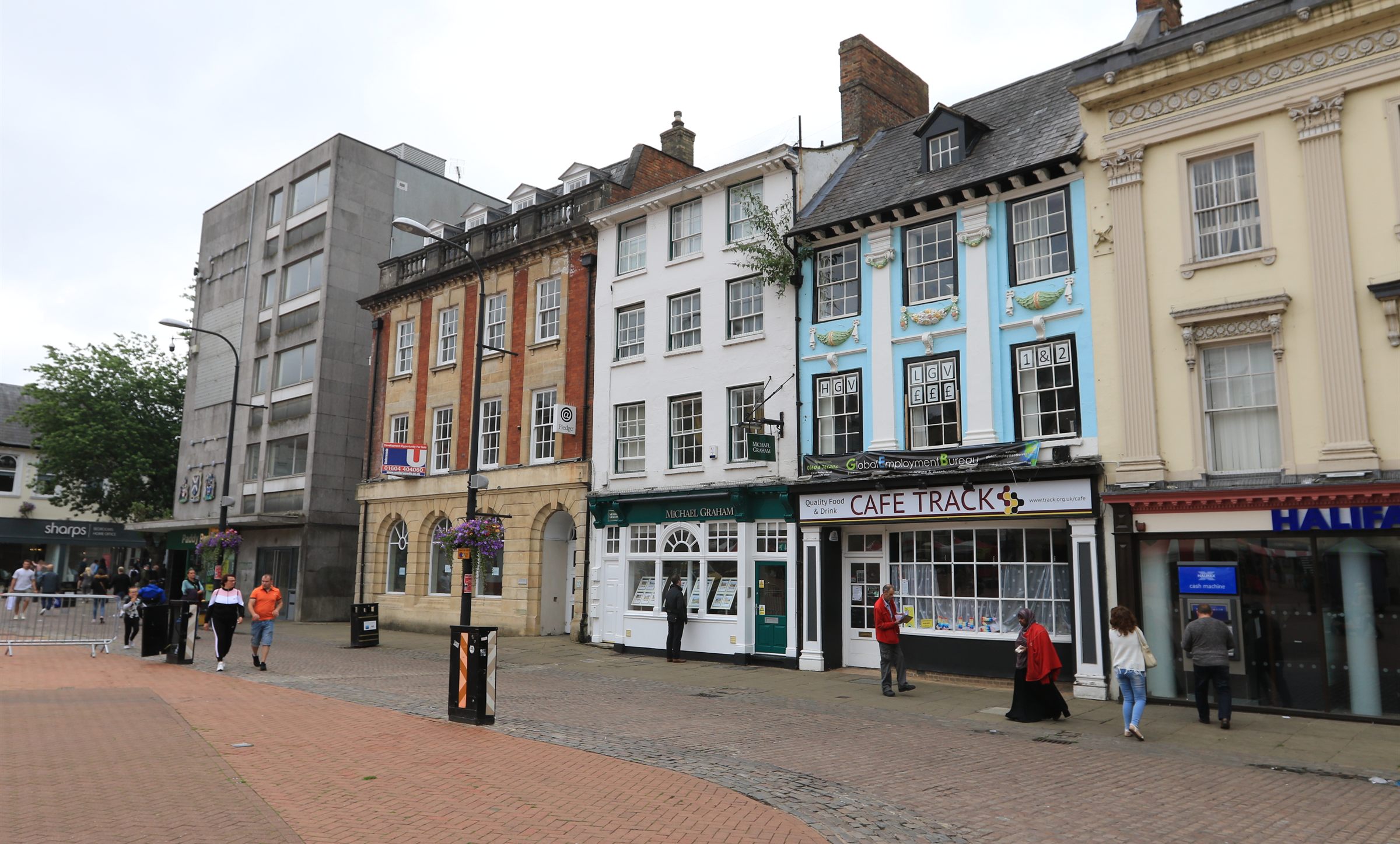 The painted Georgian frontages of Market Square in Northampton, shoppers passing the cafes beneath