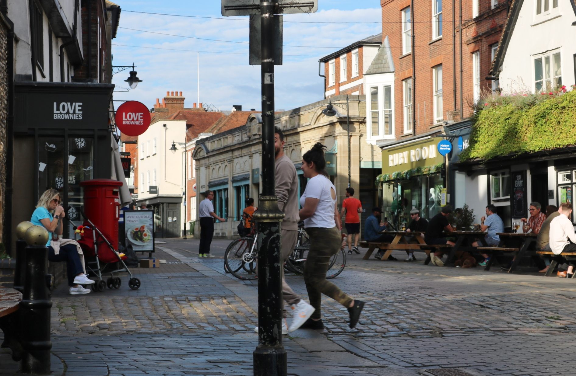 Market Place in St Albans, people crossing the cobbles past cafe benches and the old market buildings