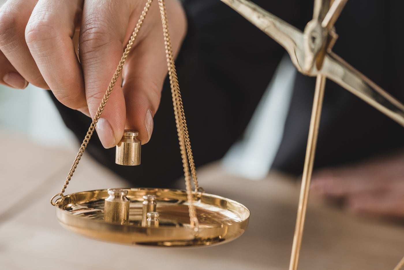 A hand placing a brass weight on a balance scale