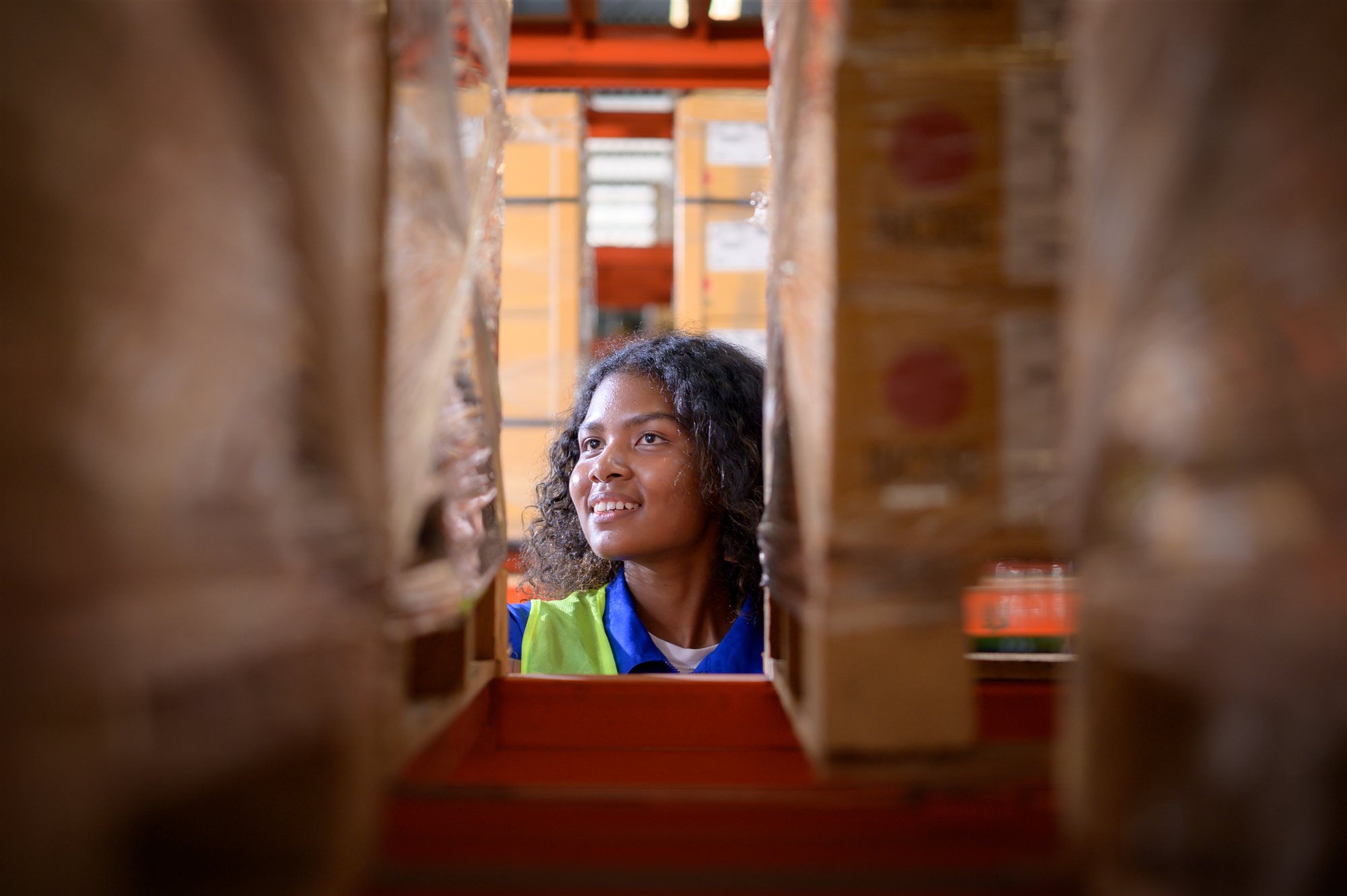 A woman in a hi-vis vest looking up between two stacked pallets of boxed aid supplies
