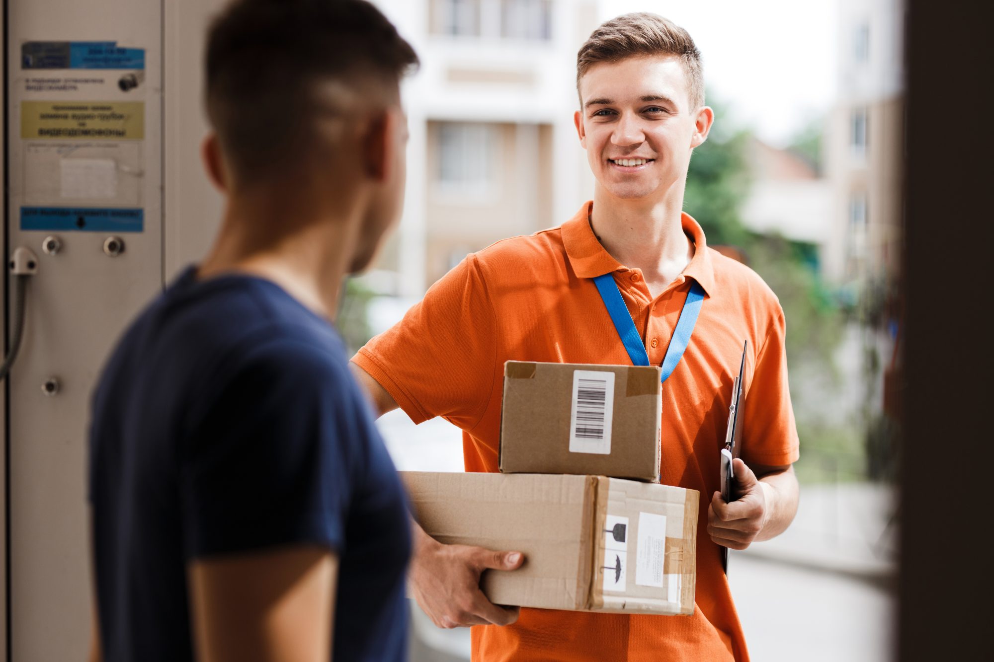 A courier in an orange polo handing two parcels to a customer at a doorway