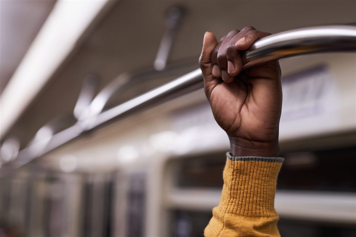 A hand in a mustard knit sleeve gripping the chrome grab rail of a moving train carriage