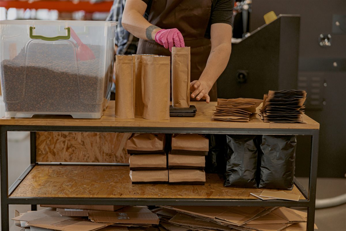 A person in an apron filling a kraft pouch with coffee beans at a packing bench