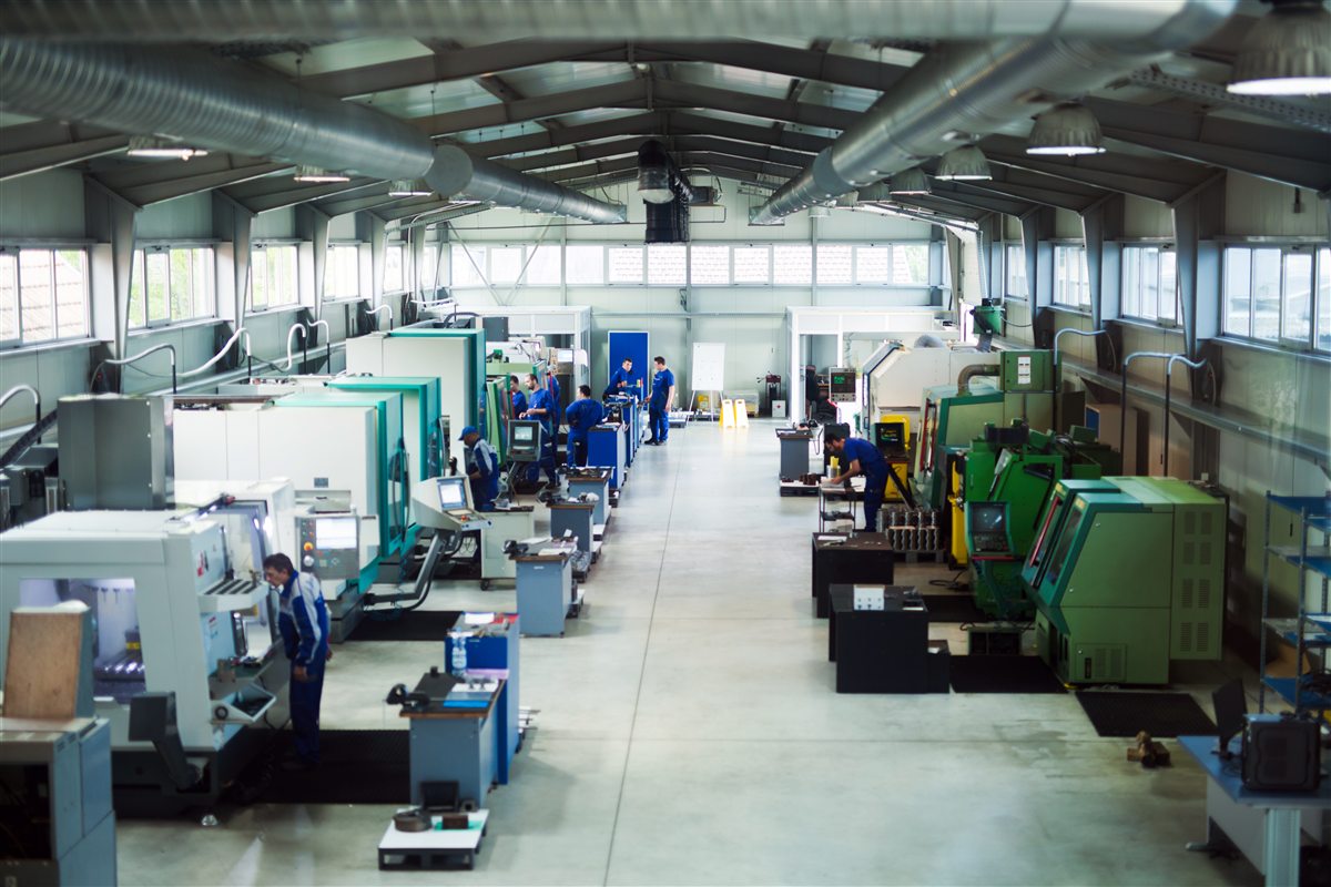 An elevated view down the centre aisle of a CNC machine shop, operators in blue overalls at the machines