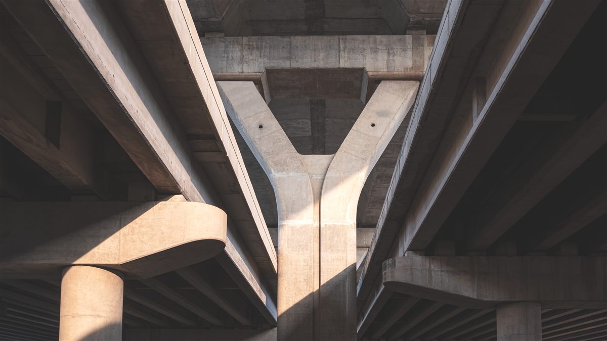 The underside of a concrete flyover, a Y-shaped pier splitting two decks in raking sunlight