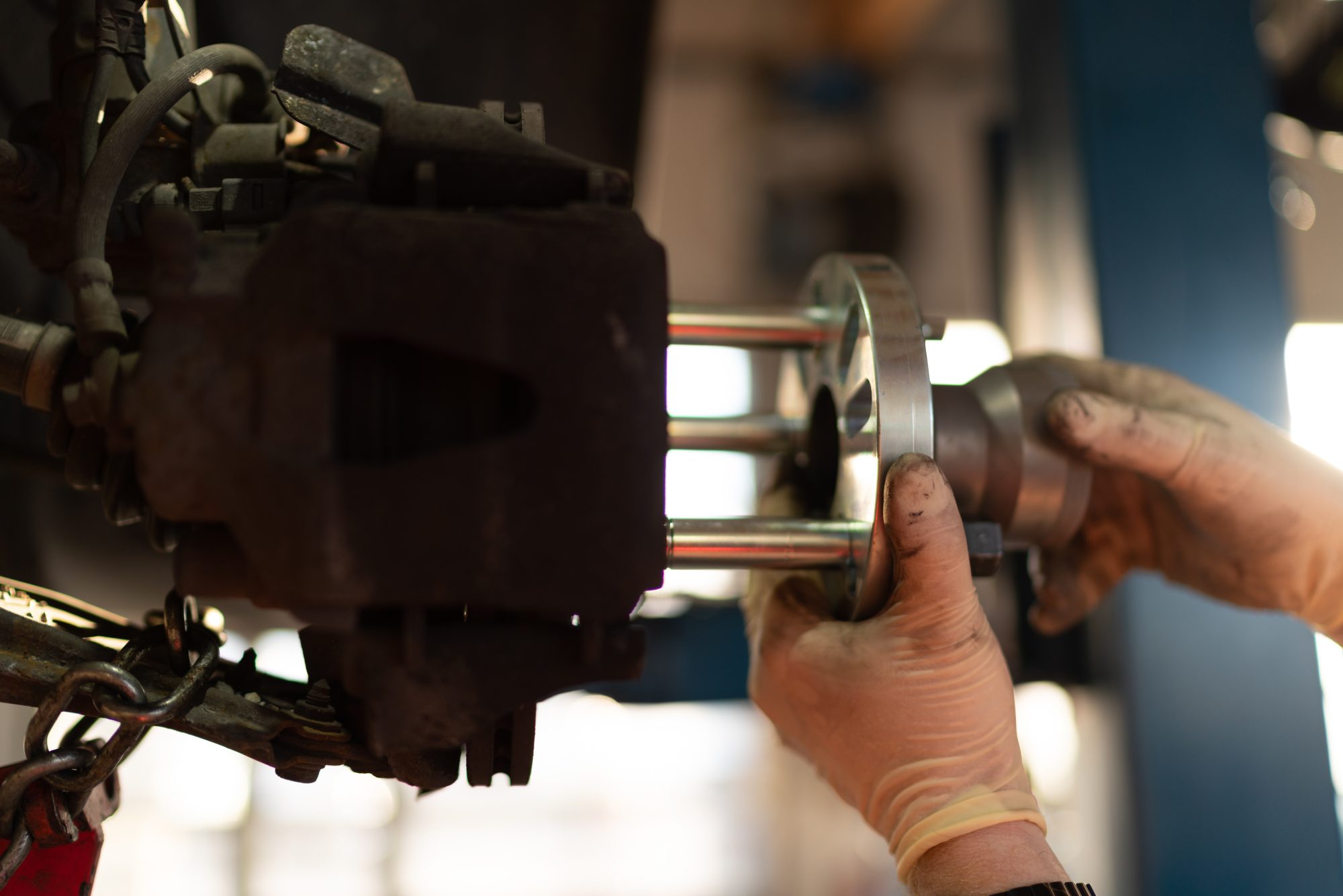 A mechanic fitting a new brake disc onto a hub, the rusted caliper assembly in the foreground
