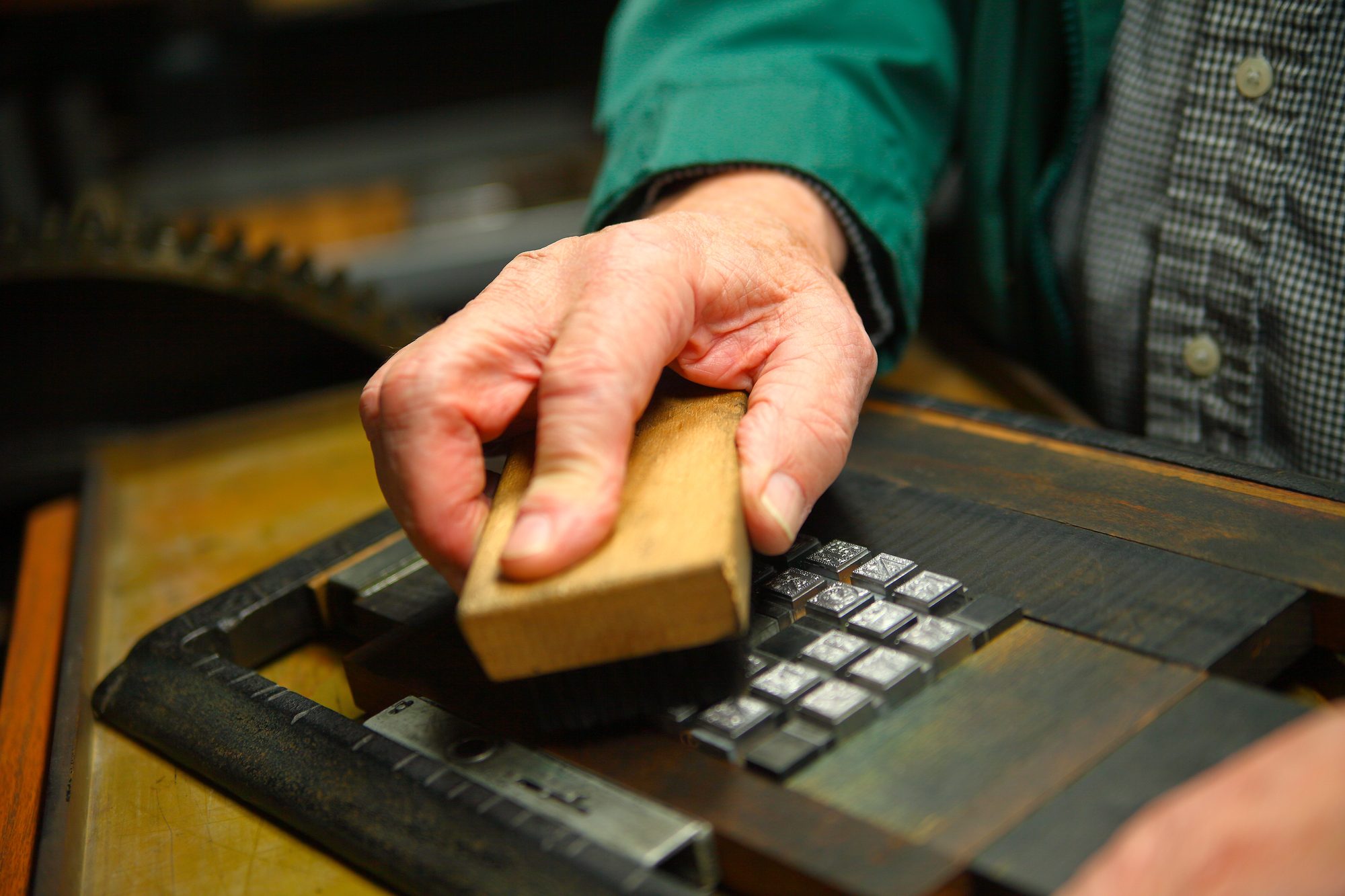 A hand pressing a wooden block onto metal letterpress type locked in a press bed