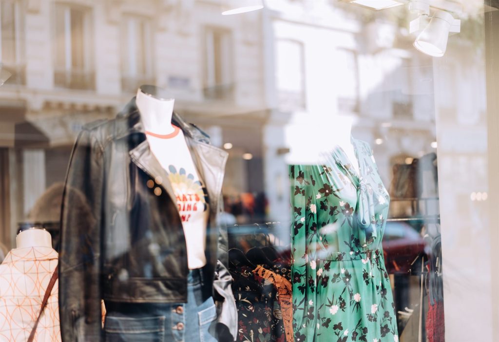 An independent boutique window seen from the pavement, a leather jacket and a floral dress on mannequins behind the glass