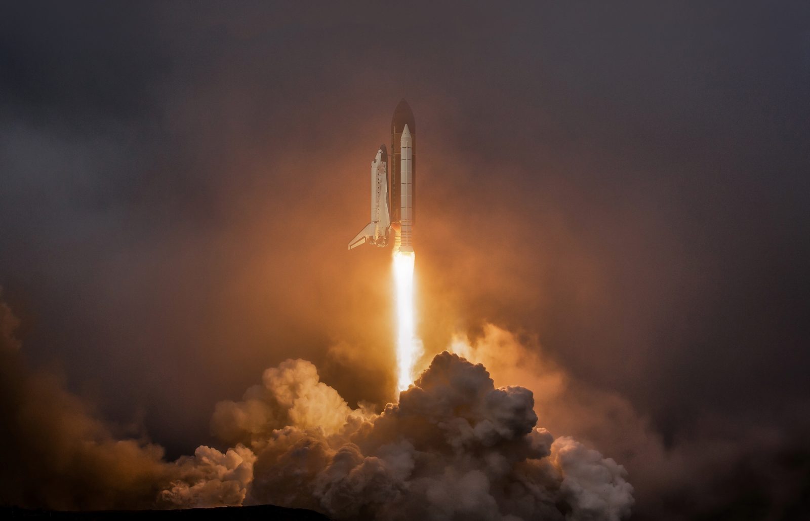 A space shuttle lifting off through its own floodlit exhaust clouds against a dark sky