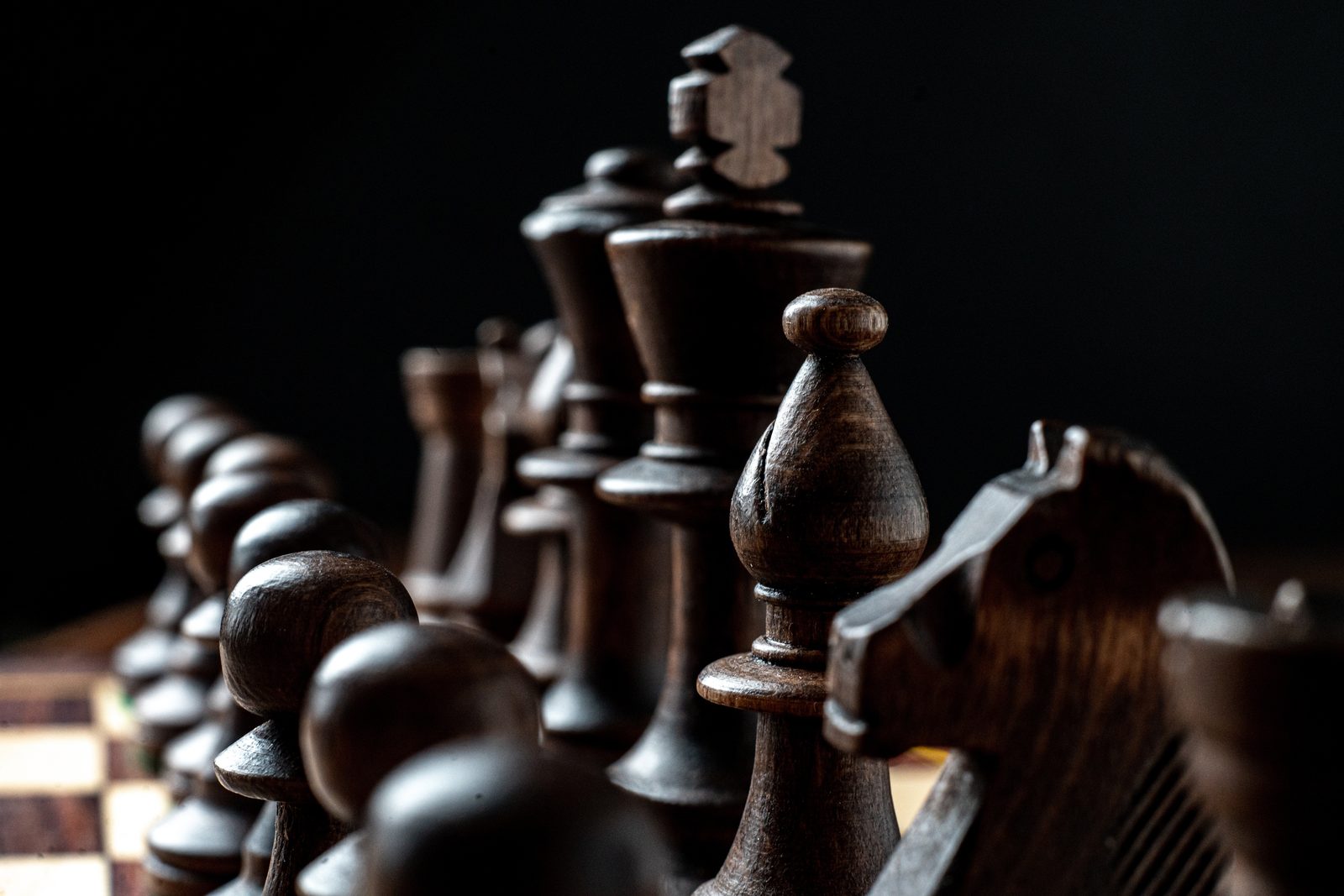 Dark wooden chess pieces in raking light, the king standing tallest