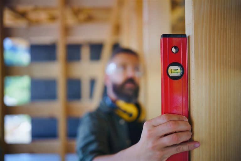 A builder checking a timber frame with a red spirit level