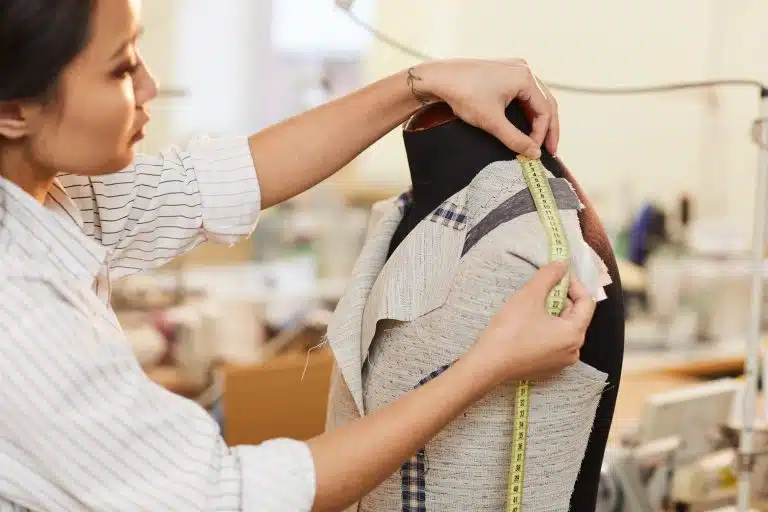 A dressmaker measuring fabric on a dress form