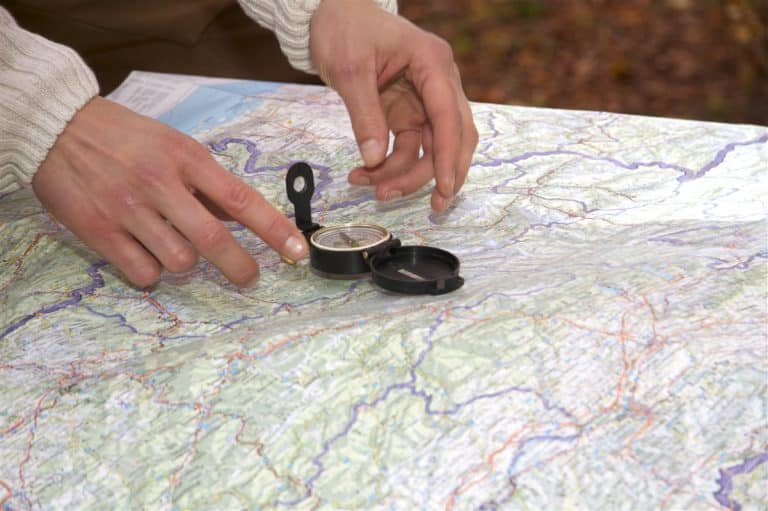 Hands placing a compass on an open paper map to plot a route