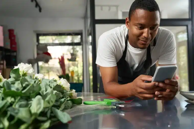 A florist leaning on the counter, reading his phone among cut flowers